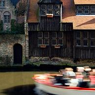 Tourists in boat and wooden rear elevation along canal in Bruges, Belgium